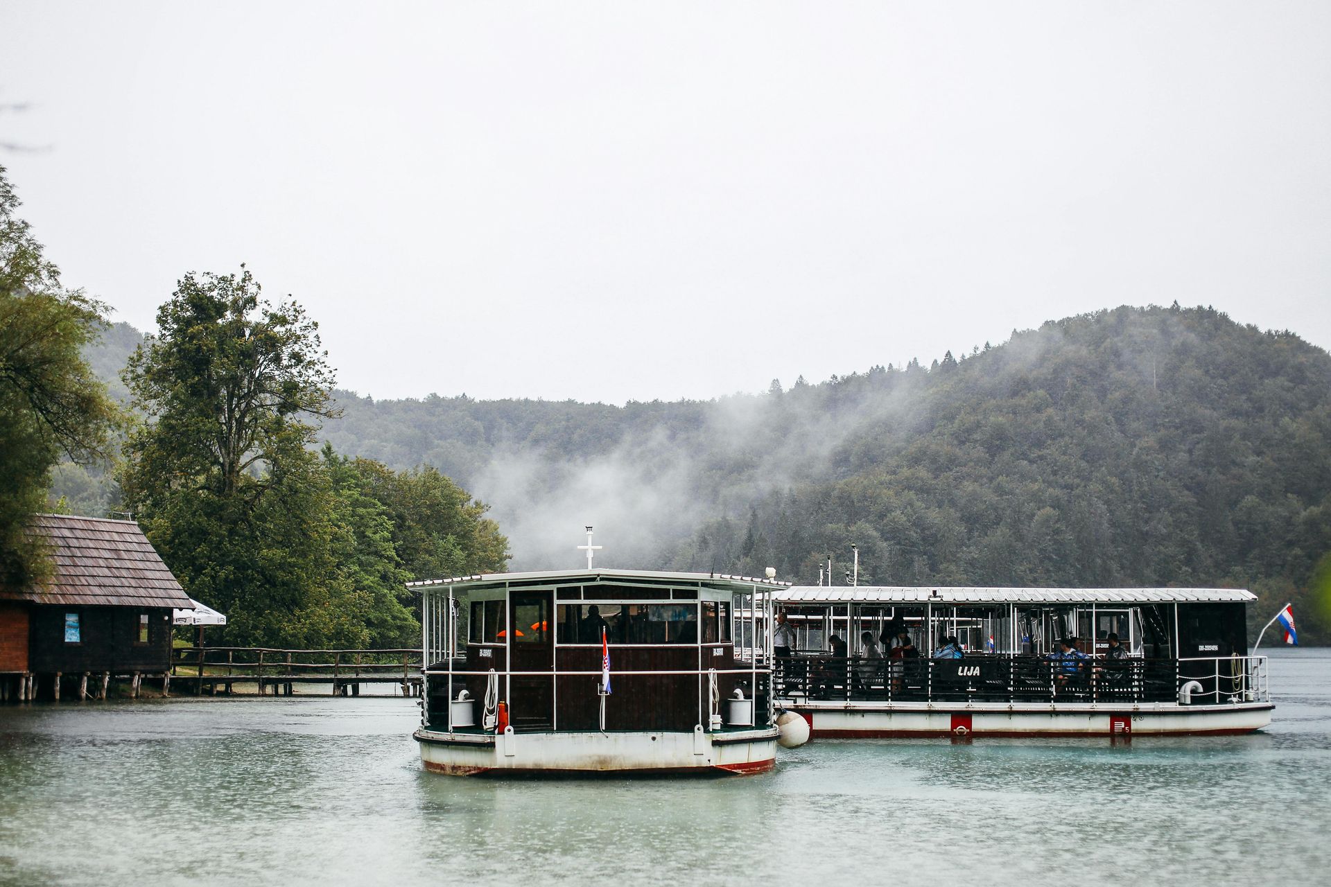 Two boats are floating on top of a lake with mountains in the background.