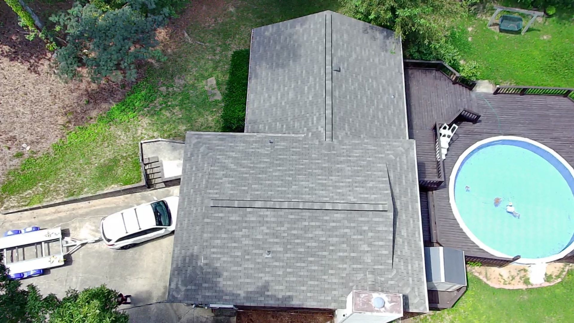 Overhead view of a house with a pool. A white van is parked near a trailer. People are in the pool.