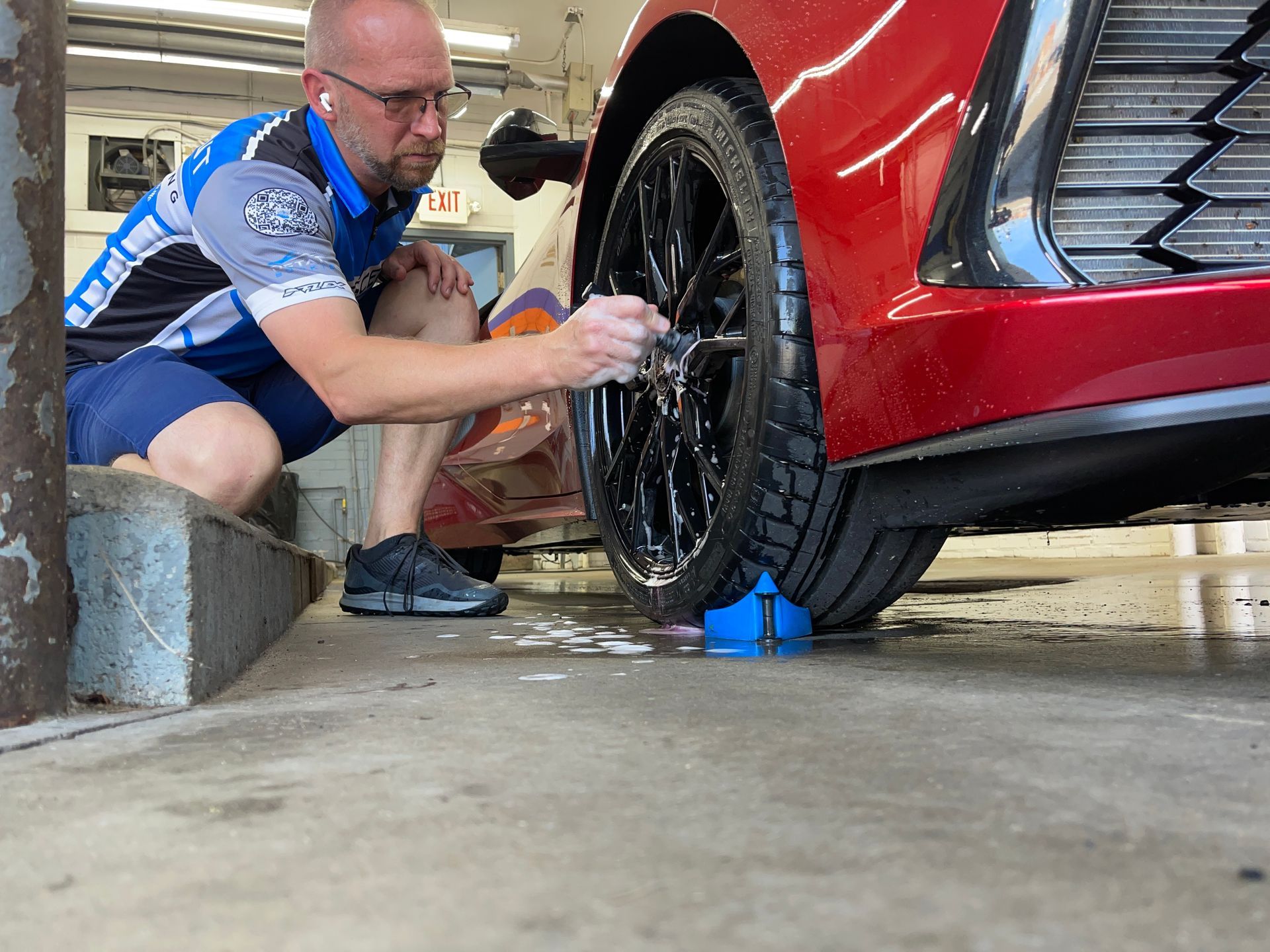 A man is cleaning the wheel of a red car in a garage.