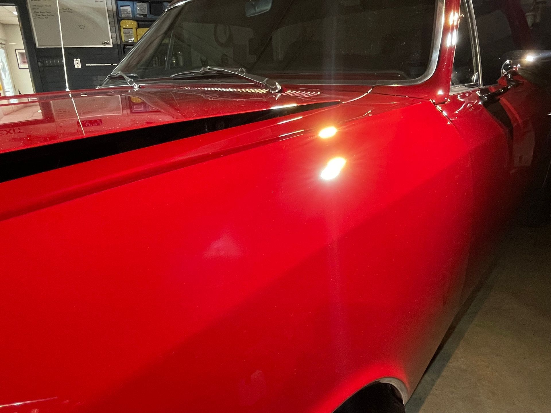 A red car is parked in a garage with the hood up.