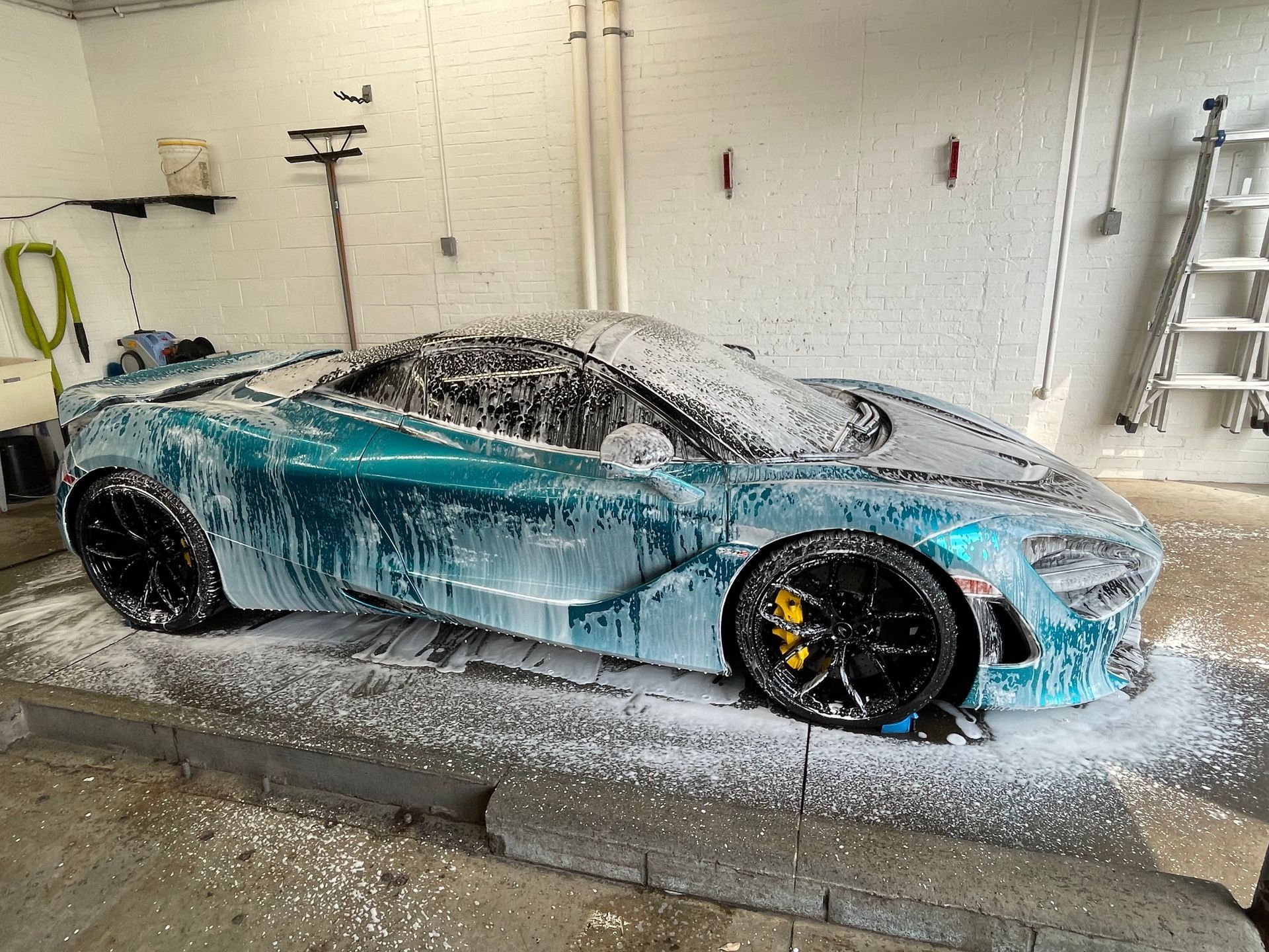 A blue sports car is covered in foam in a garage.