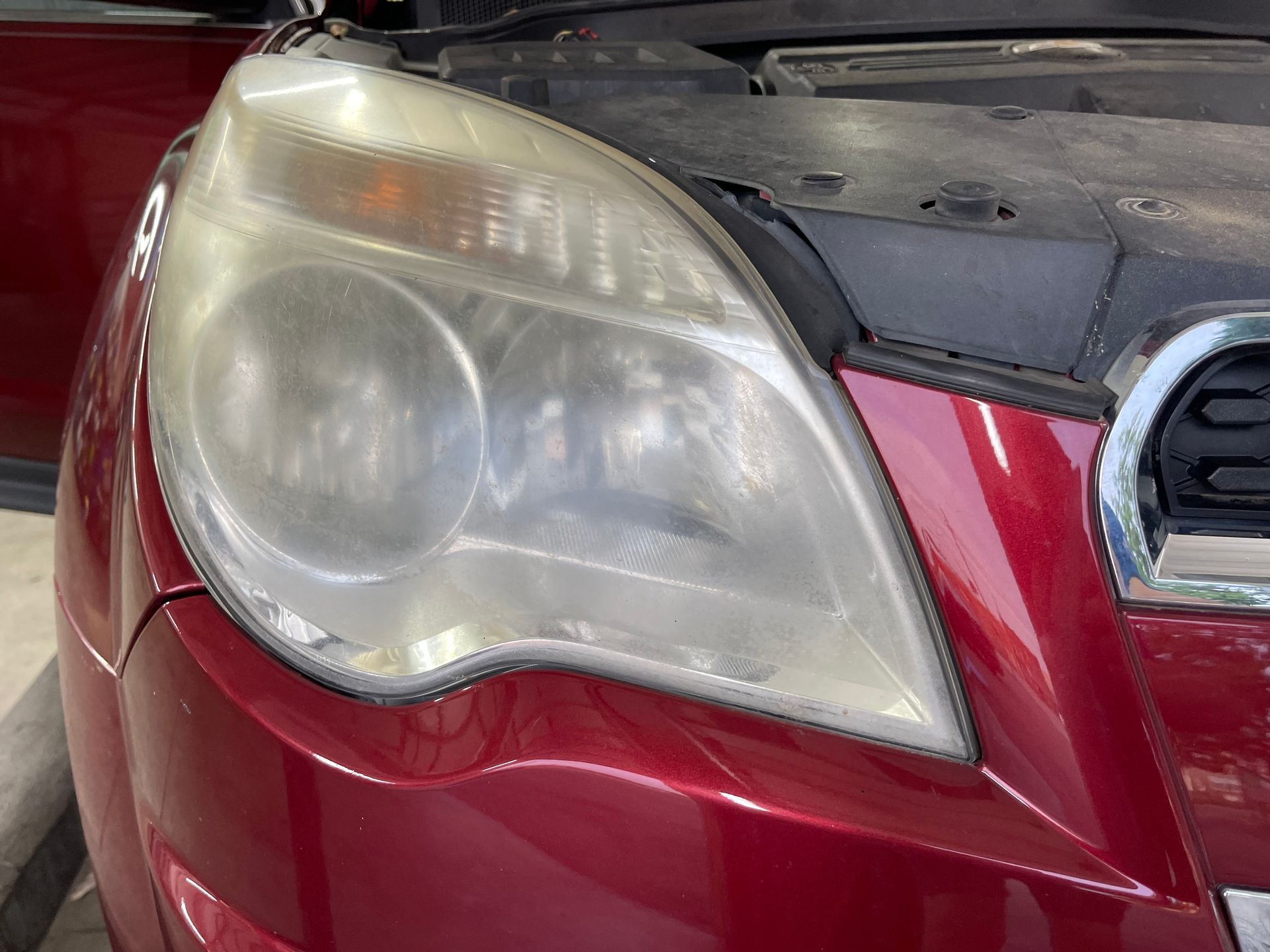 A close up of a red car 's headlight with the hood open.