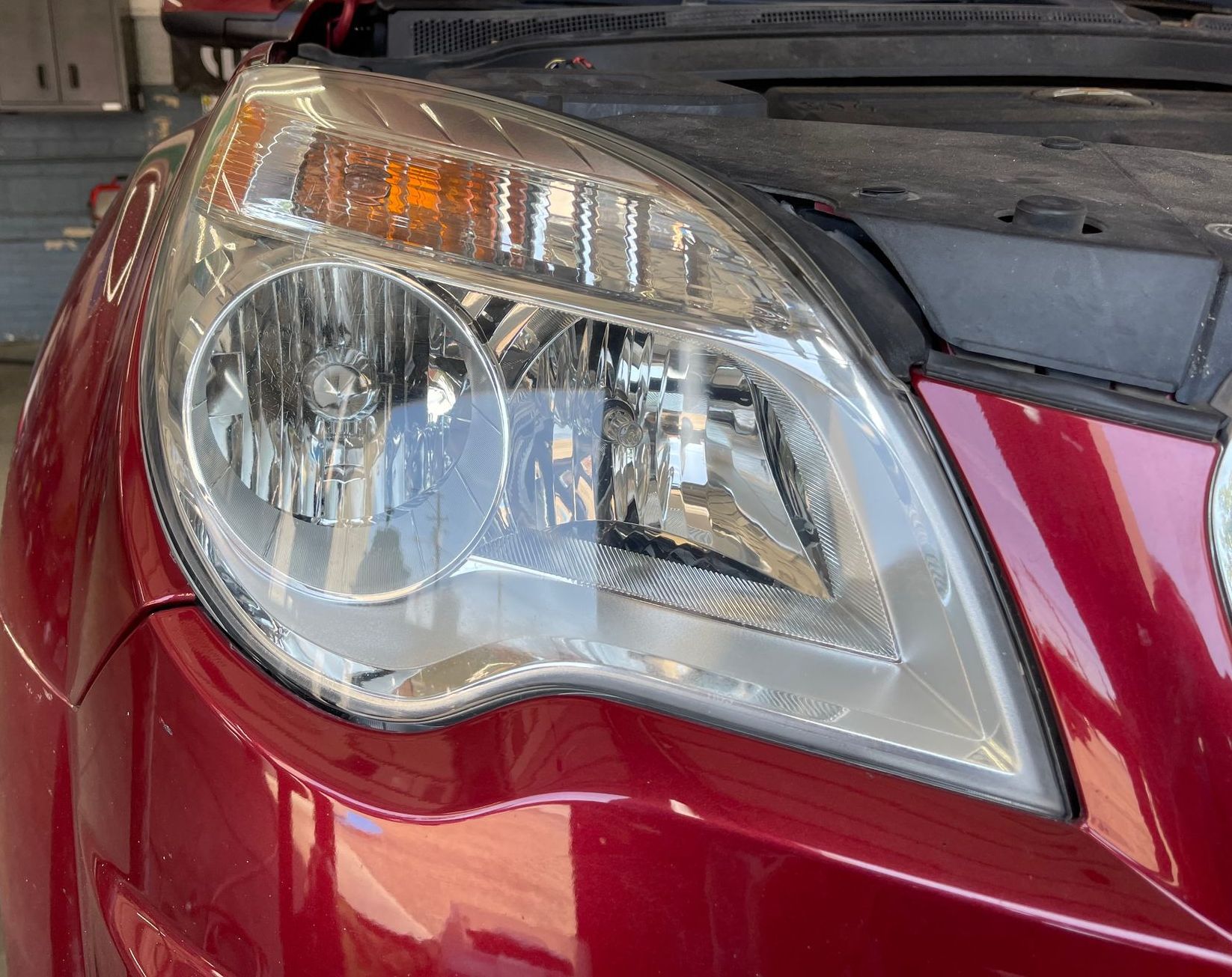 A red car with the hood up is parked in a garage.