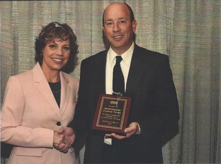 A man and woman shaking hands while holding a plaque