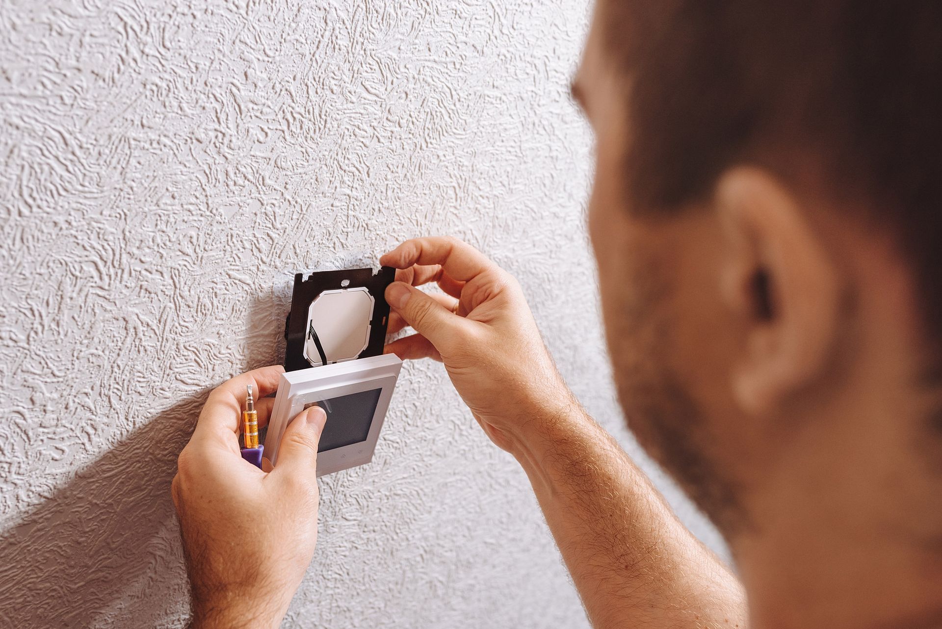 A man is installing a thermostat on a wall.