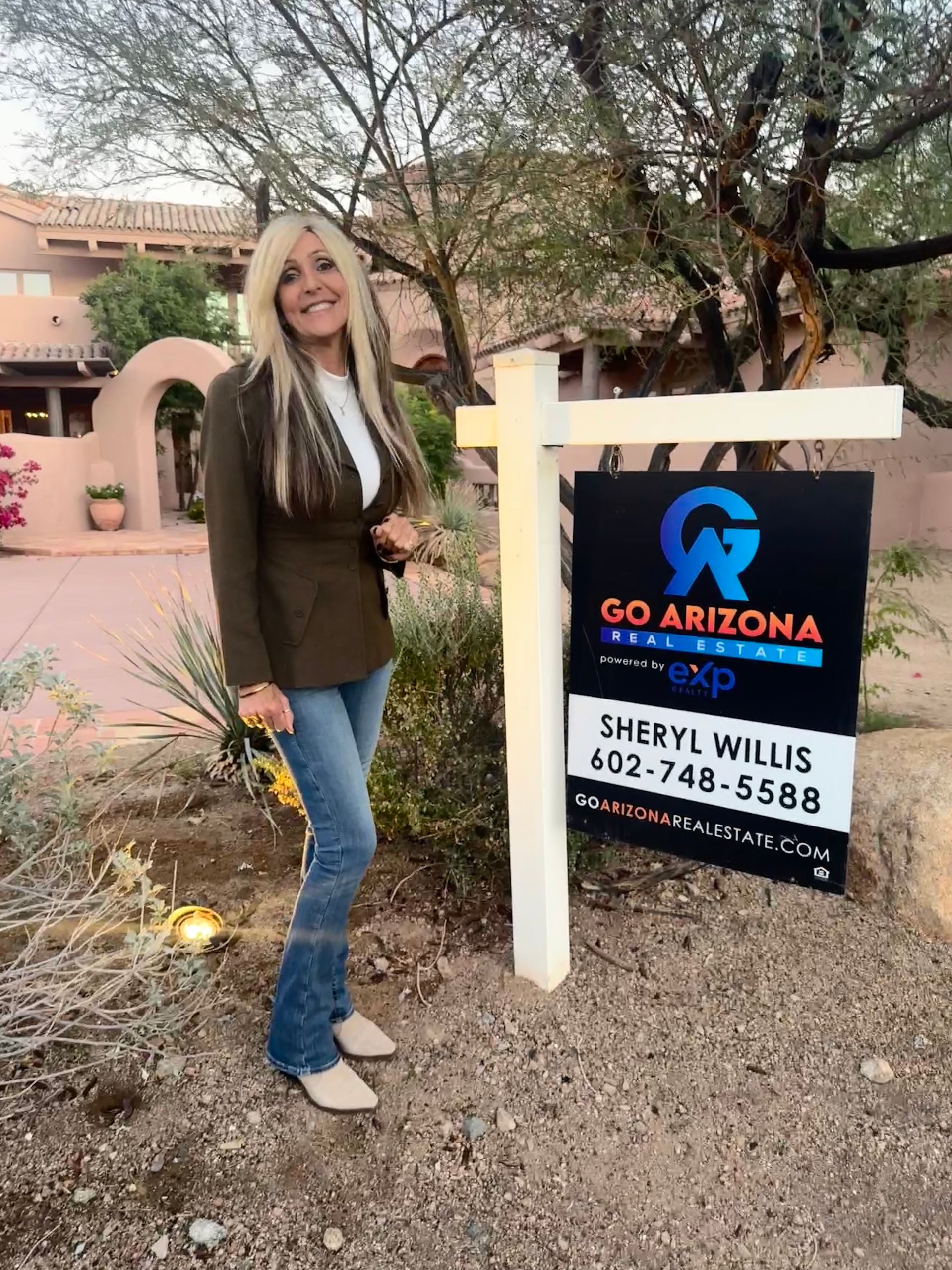 A woman is standing in front of a real estate sign.