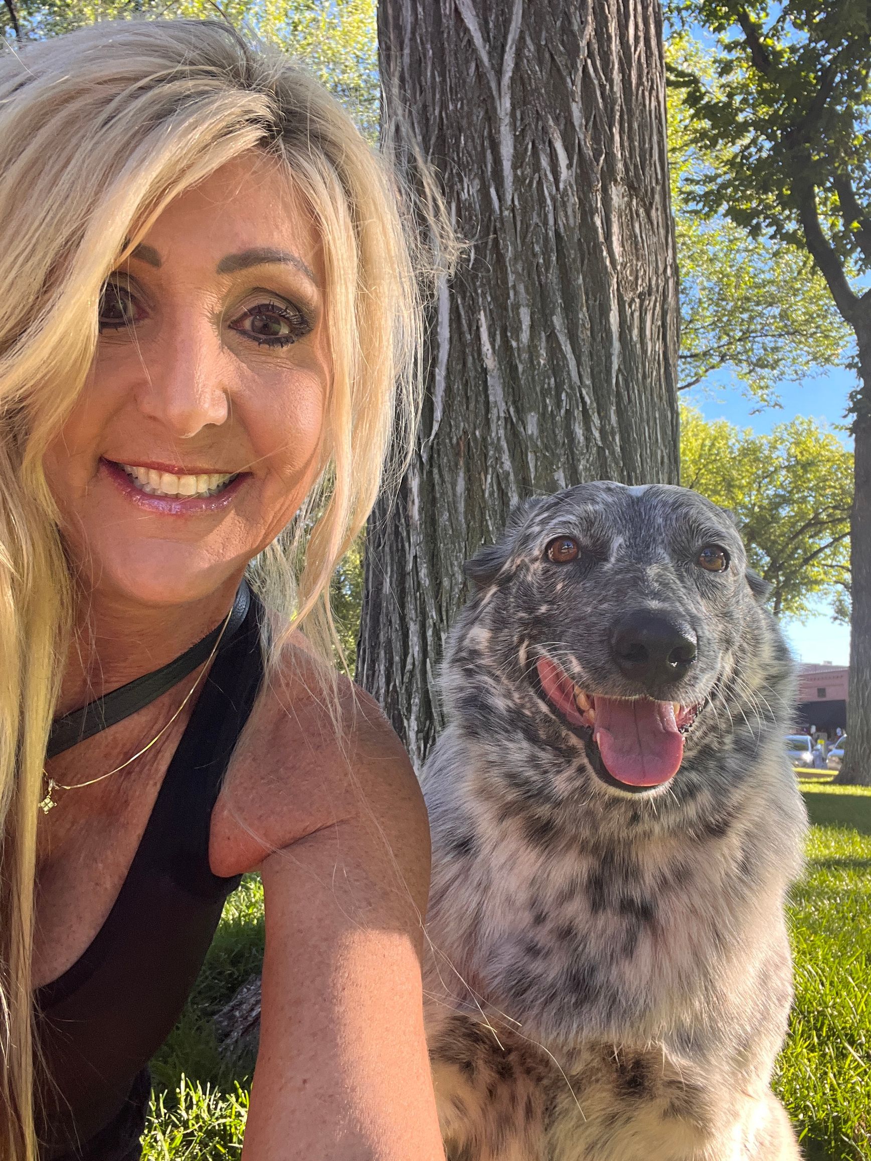 A woman is posing for a picture with her dog in front of a tree.