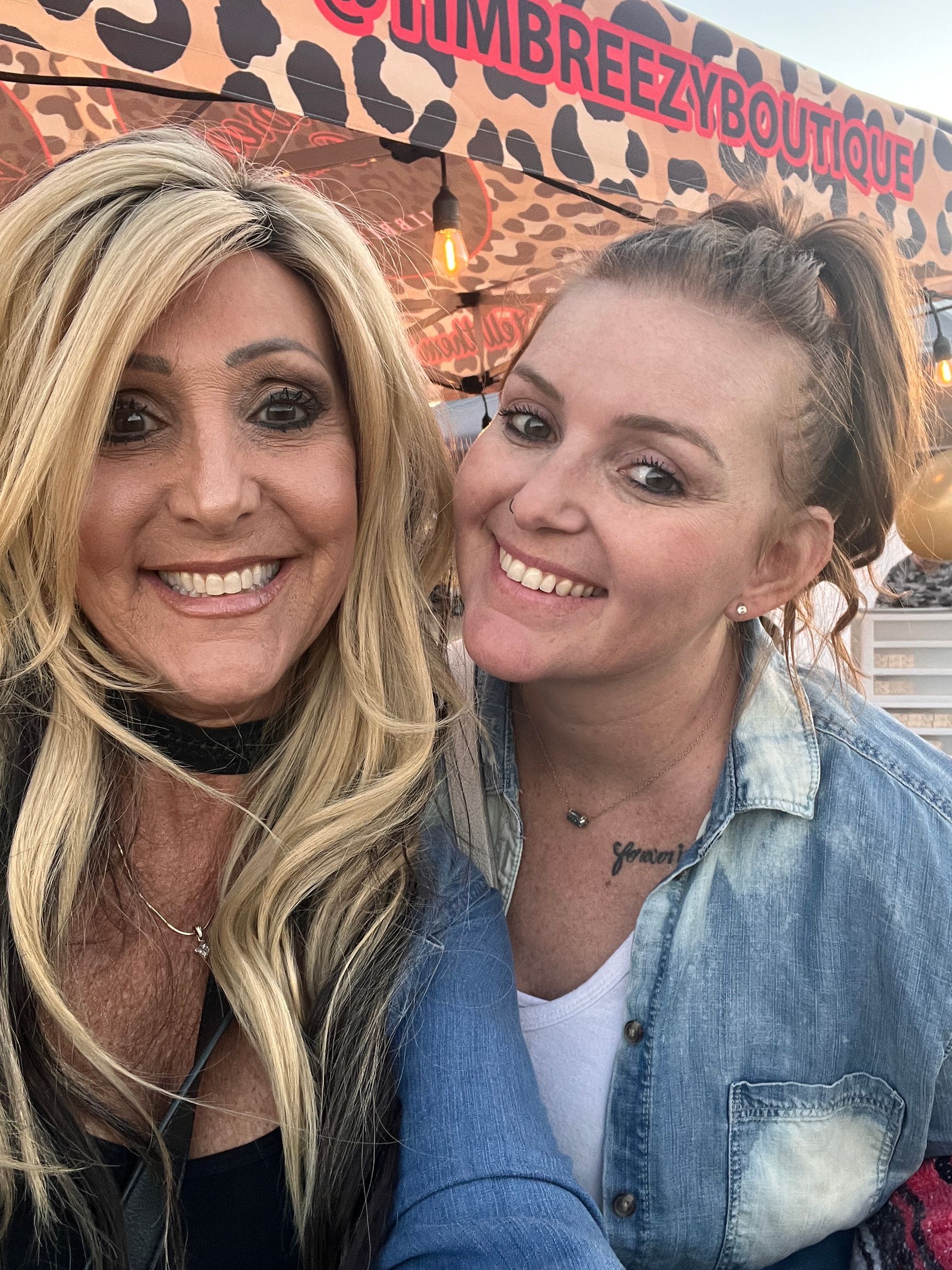 Two women are posing for a picture in front of a leopard print sign.