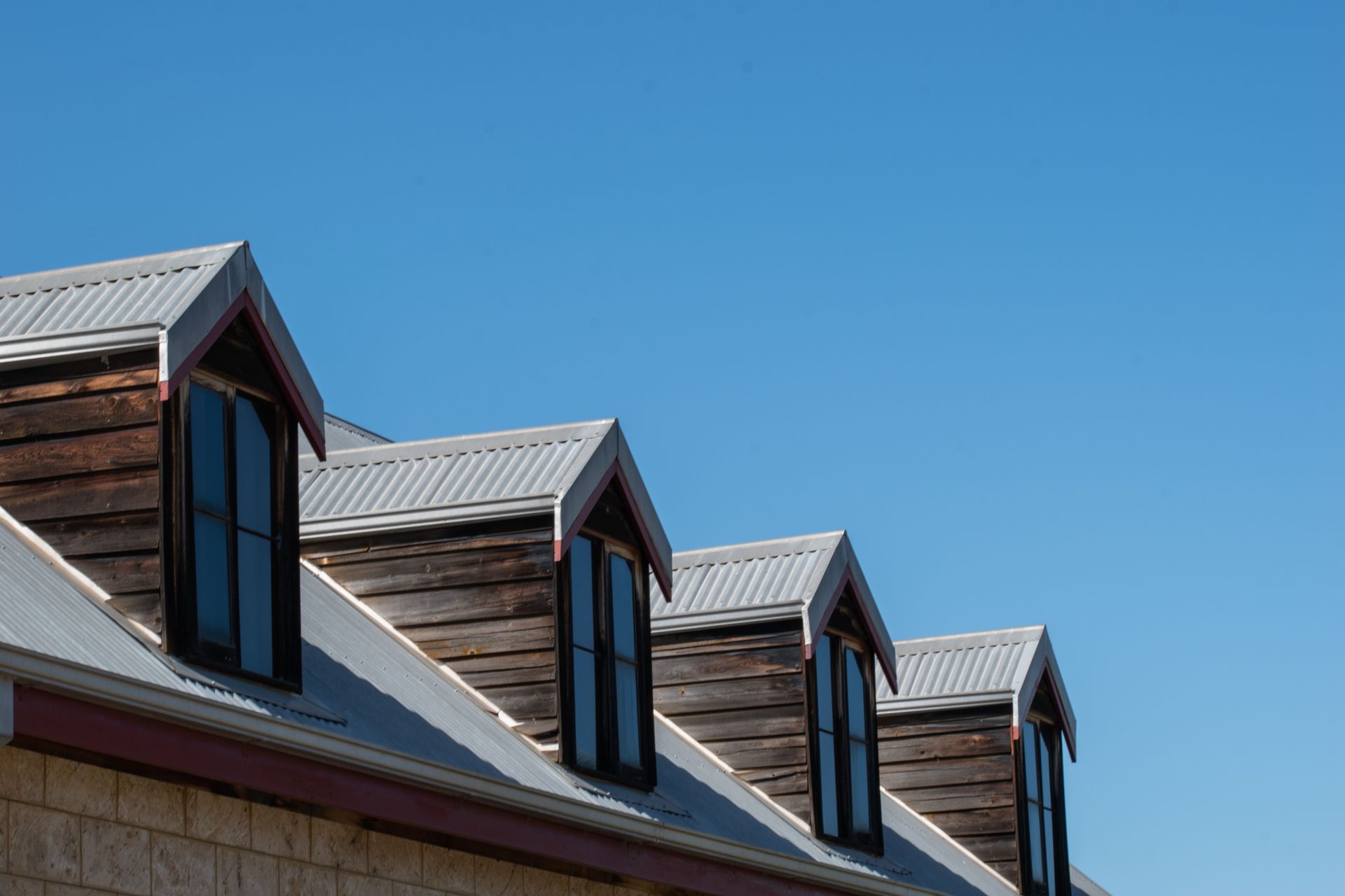 Three dormer windows with gray roofs on a building against a clear blue sky
