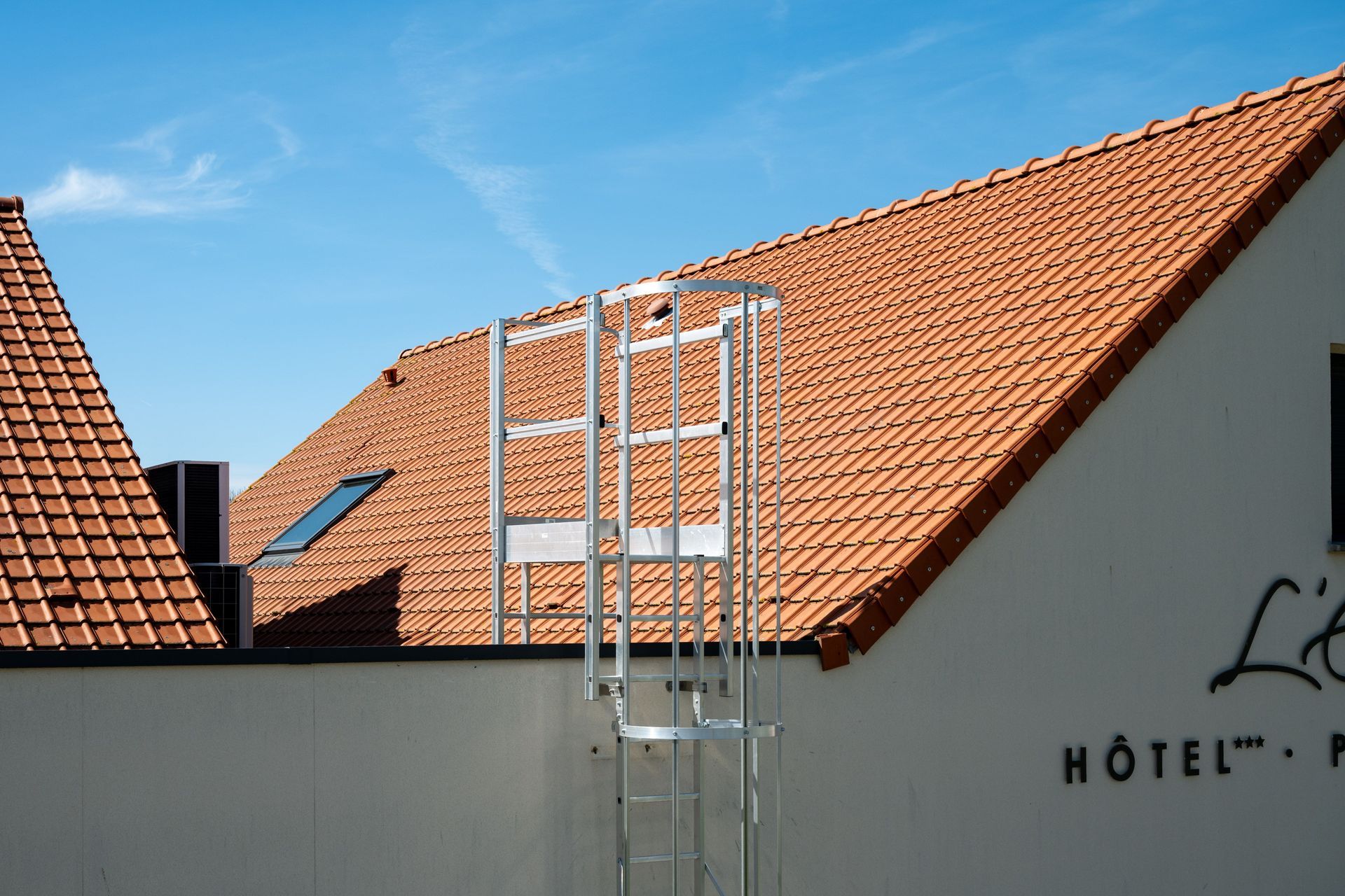 Rooftops with red tiles and a metal ladder against a hotel building under a clear sky