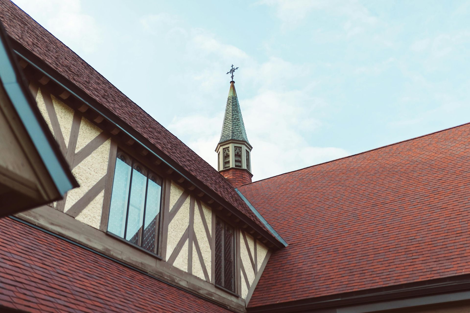 Red-tiled church roof and steeple with cross against a blue sky