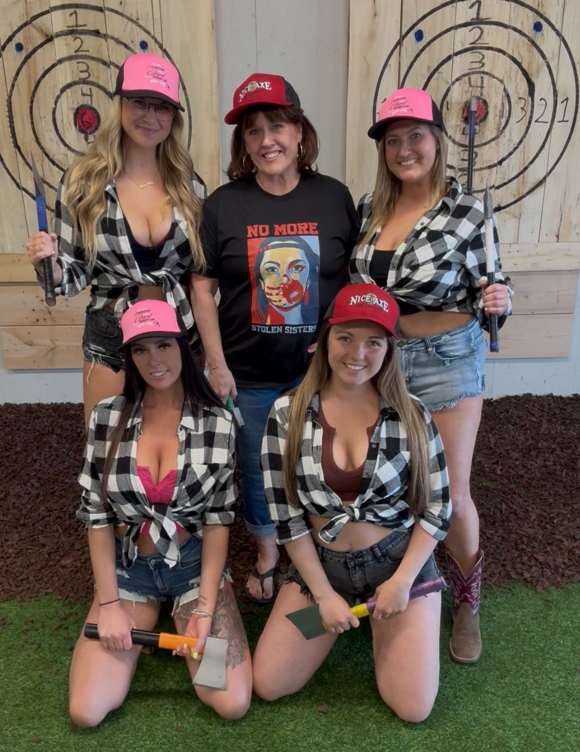 A group of women are posing for a picture while holding axes in front of a target.