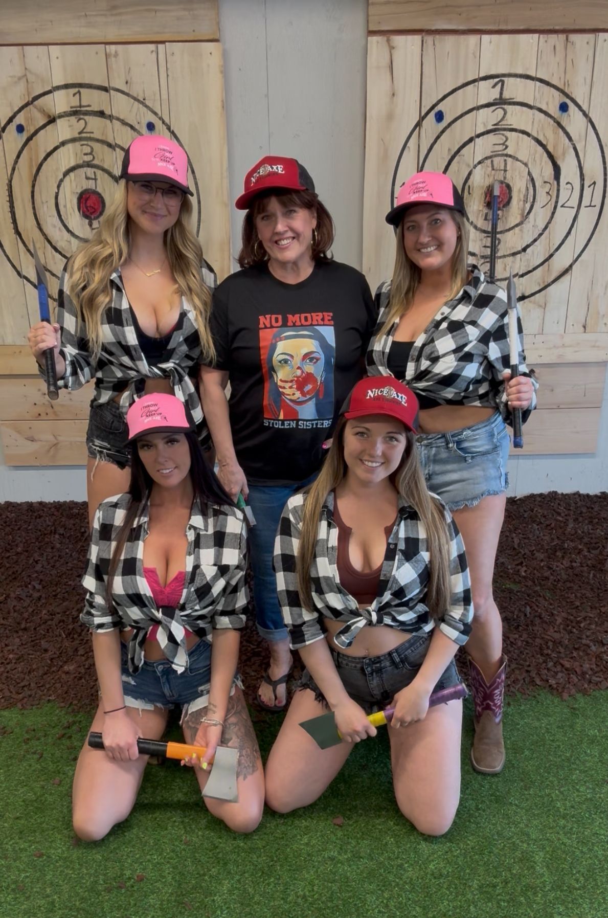 A group of women are posing for a picture while holding axes in front of a target.