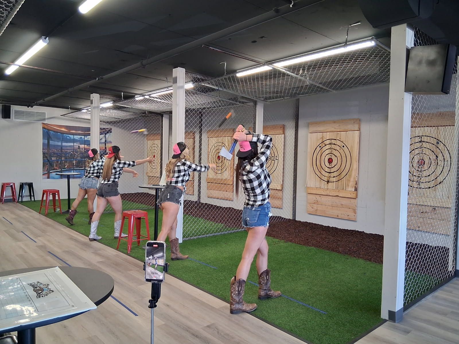 A group of women are throwing axes in a room with a lot of targets.