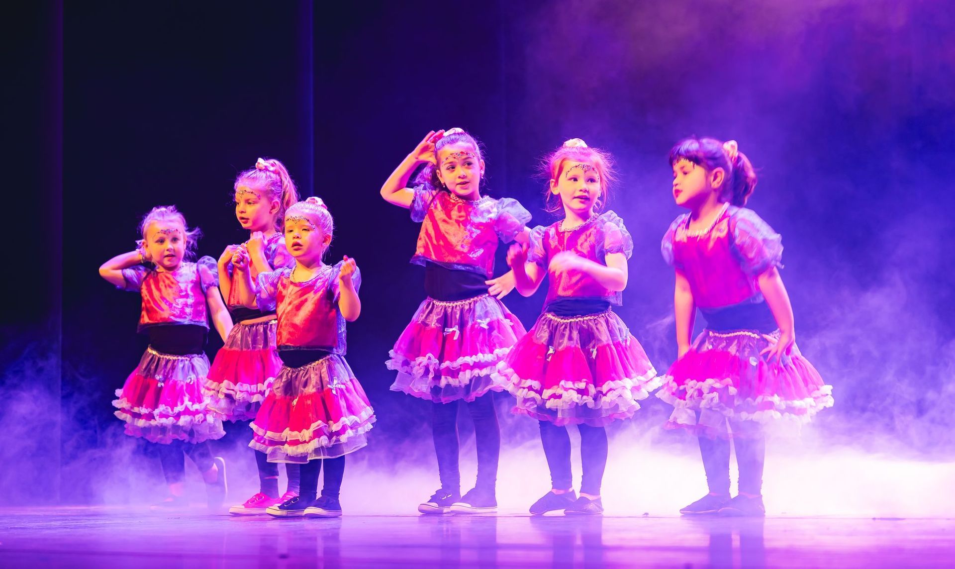 Twee vrouwen doen sit-ups op roze matten in een sportschool. De ene lacht, de andere helpt.