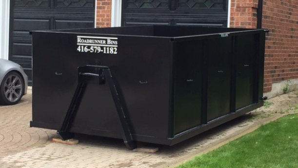 a dumpster for roadrunner bins sits in front of a garage