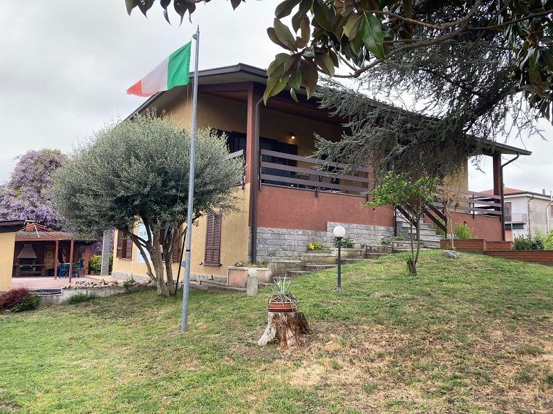 Casa con bandiera italiana, balcone in legno e prato verde.