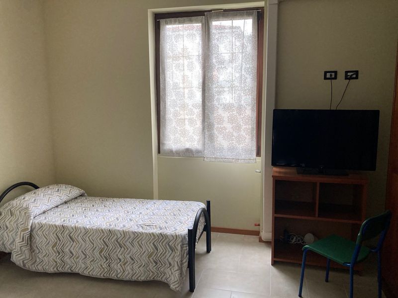 Una semplice camera da letto con un letto, una TV e una finestra con una tenda a fantasia.