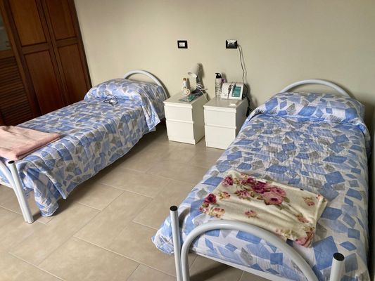 Due letti con copriletti floreali blu, comodini e un ventilatore in una stanza.