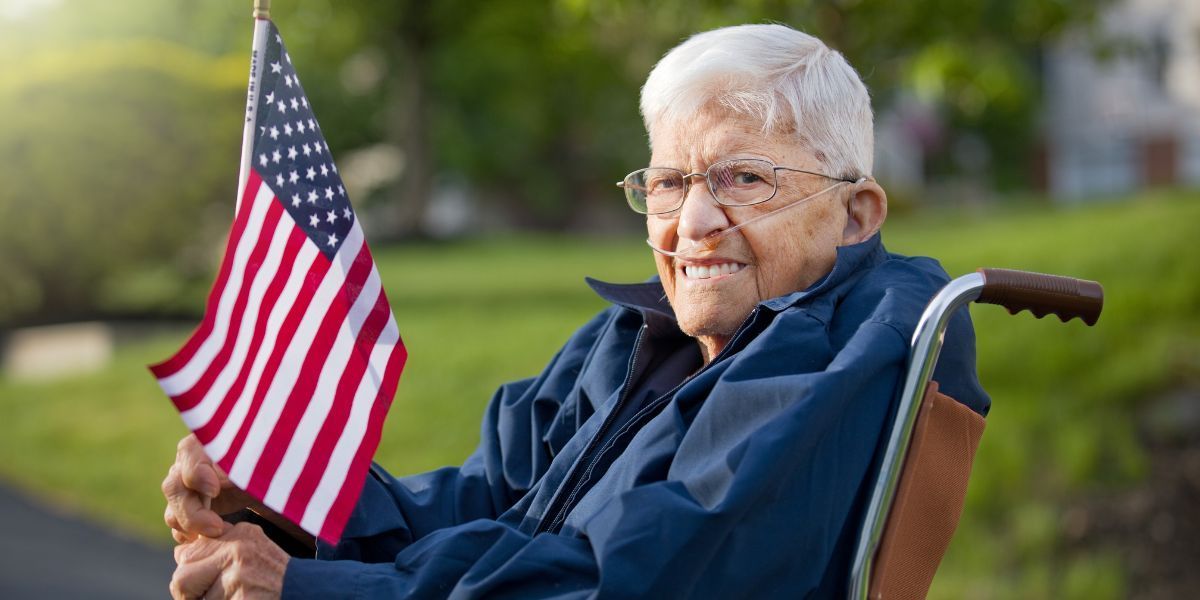 An elderly man in a wheelchair is holding an american flag.