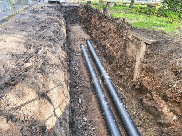 Two black pipes are laying in the dirt in a trench.