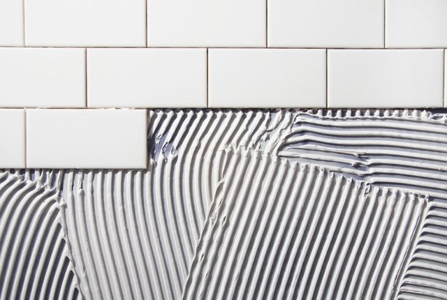 A close up of a tile being applied to a wall.