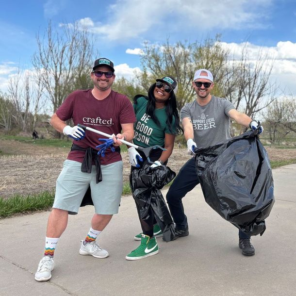 Two men and a woman helping clean up trash along a walkway. It's a sunny, beautiful day, and they are smiling and having fun during a Doozy Donates volunteer project. 