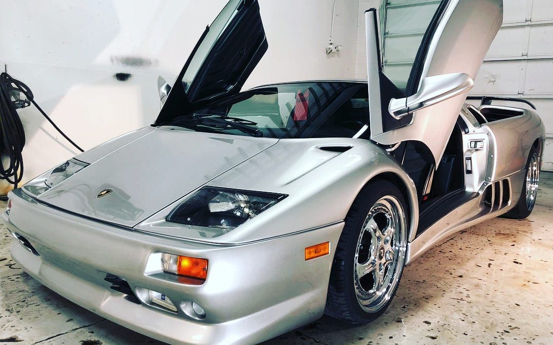 A silver sports car is parked in a garage with its doors open