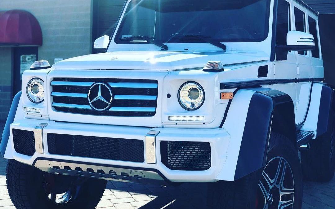 A white mercedes benz g500 is parked in front of a building.