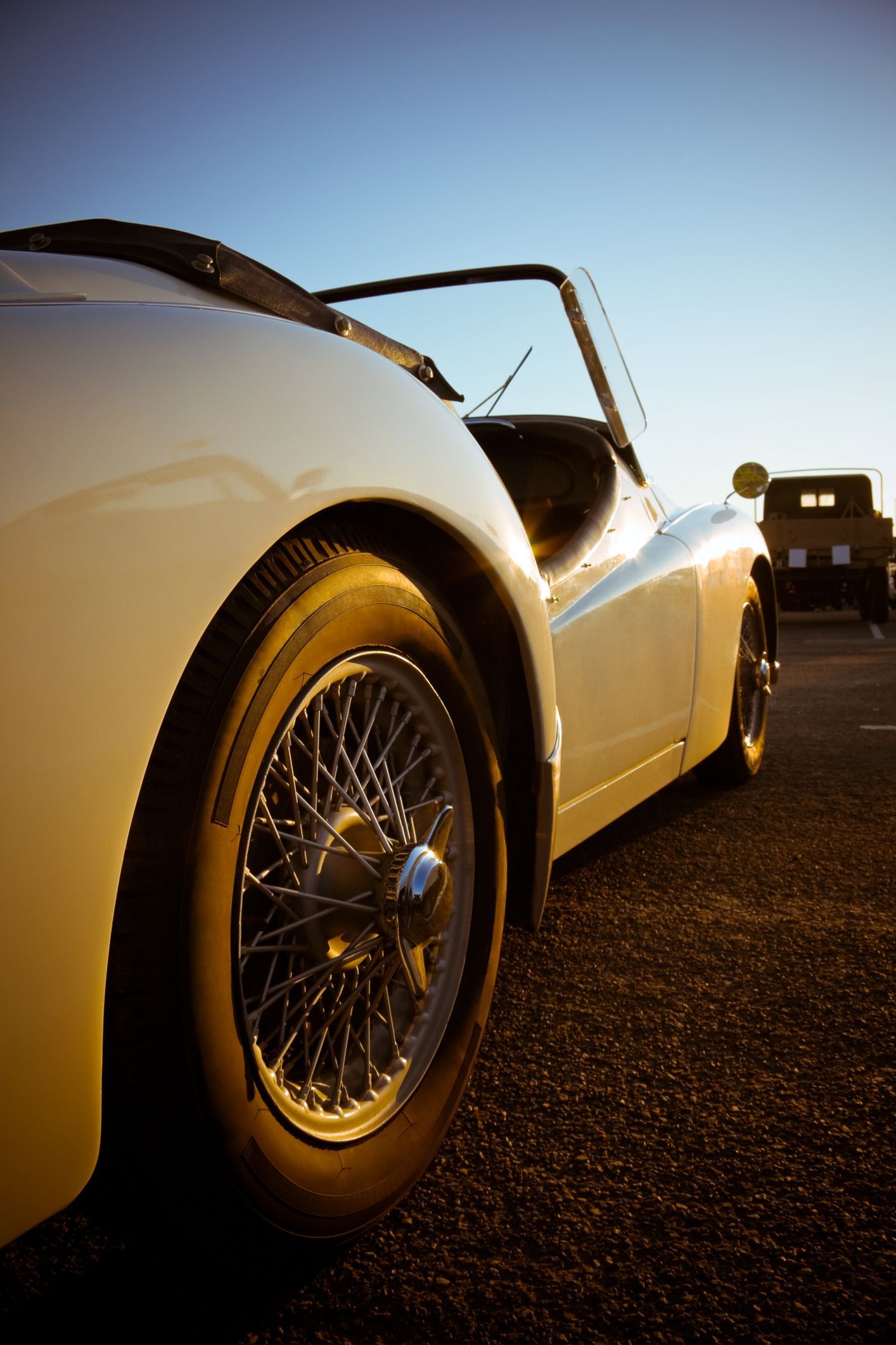 Cream-colored classic convertible car on asphalt with wire wheels, against a blue sky.