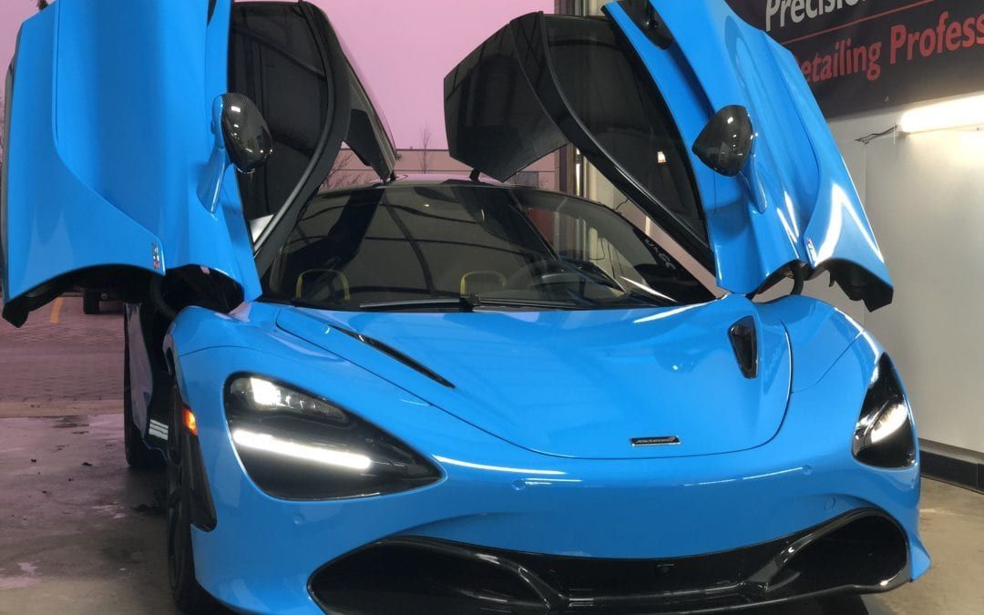 A blue sports car with its doors open is parked in a garage.