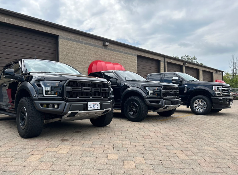 Three black ford trucks are parked in front of a garage.
