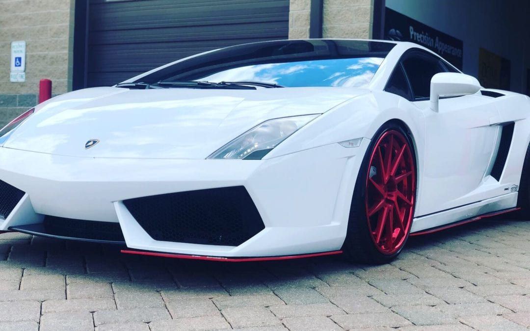 A white lamborghini with red wheels is parked in front of a garage.