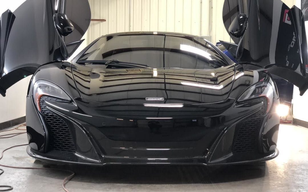 A black sports car is parked in a garage with its doors open.