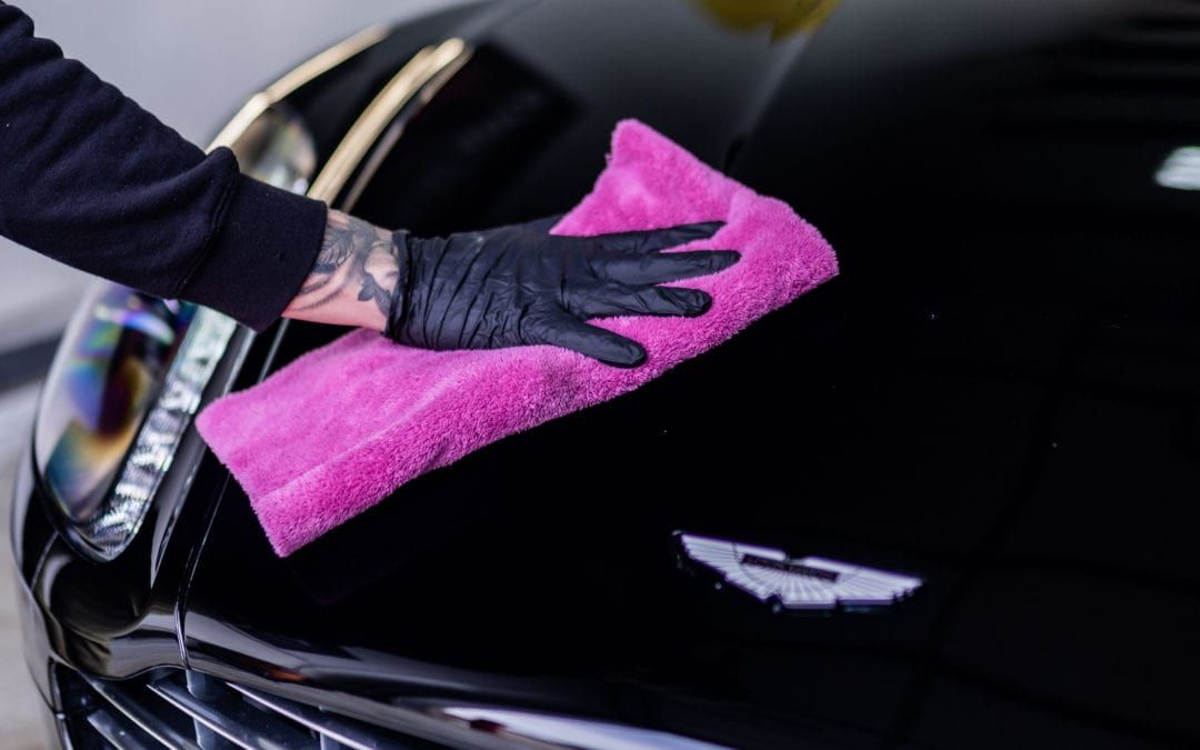 A person is cleaning a black car with a pink towel.