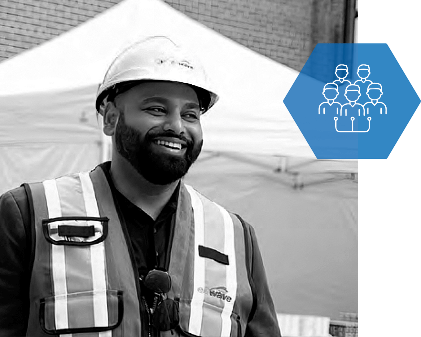 A man wearing a hard hat and safety vest is smiling in a black and white photo.