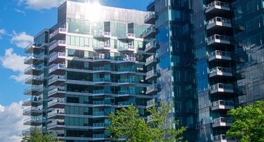 A tall building with a lot of windows and balconies is surrounded by trees.