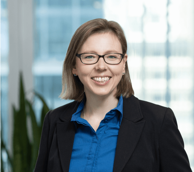 A woman wearing glasses and a blue shirt is smiling for the camera.