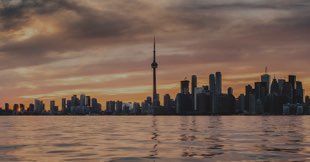 A city skyline is reflected in the water at sunset.