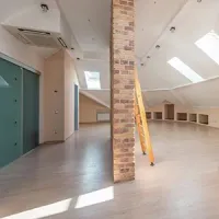 Empty loft interior with brick pillar, skylights, gray floor, and ladder near built-in cubbies