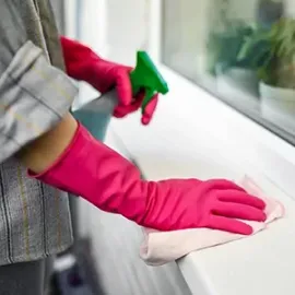 Person in pink gloves cleaning a white windowsill with a cloth and spray bottle
