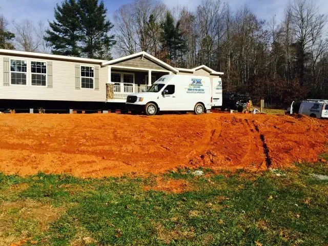 A person in a black t-shirt and work gloves repairs internal wiring in a wall-mounted heating unit near plumbing pipes.