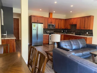 Cocina moderna y sala de estar con gabinetes de madera, electrodomésticos de acero inoxidable y un sofá de cuero azul.