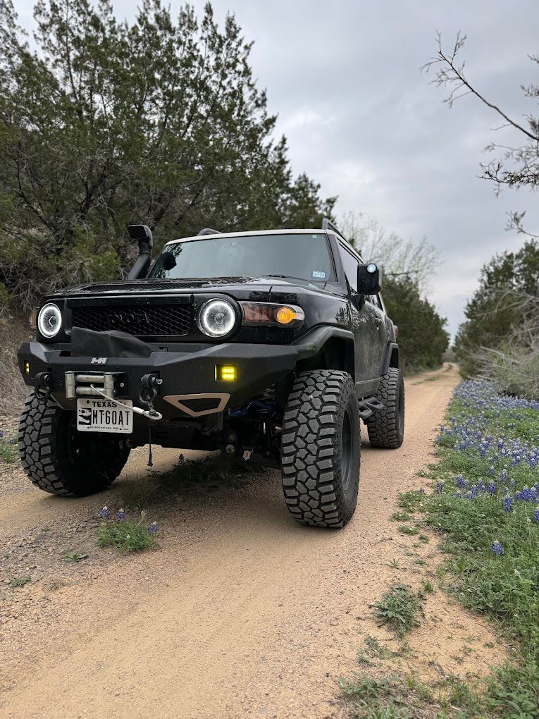 A black SUV on lifted wheels drives down a country road.