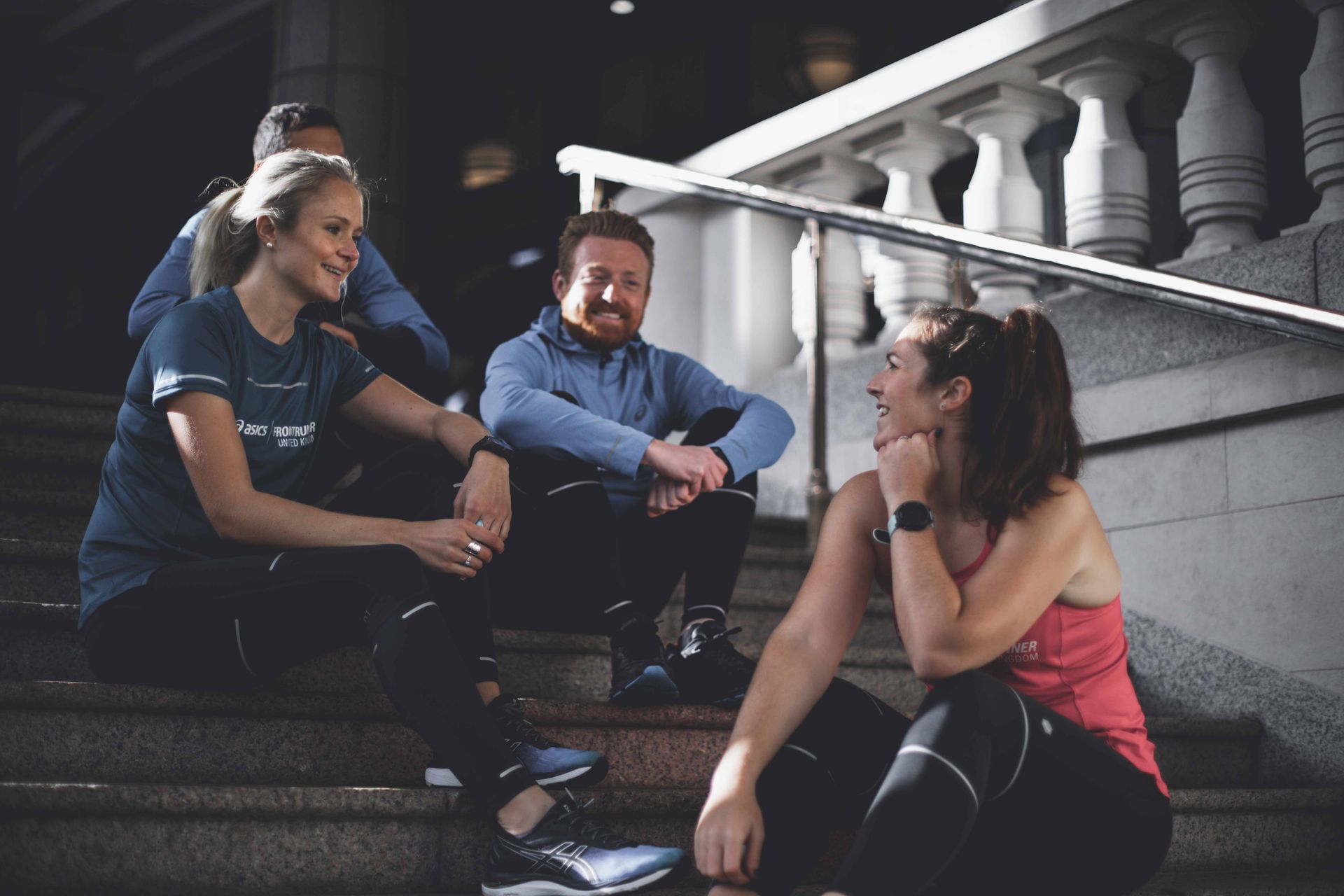 Een groep hardlopers in sportkleding rust uit op stenen trappen, lachend en pratend.