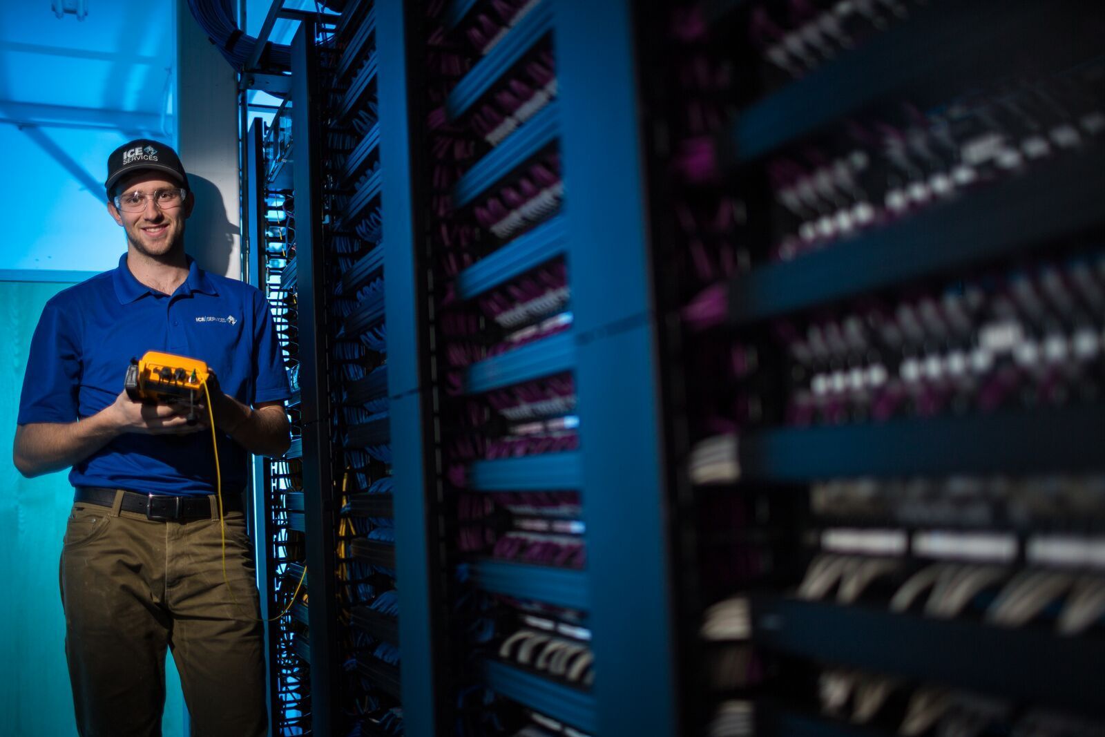 A man is standing in a server room holding a device.