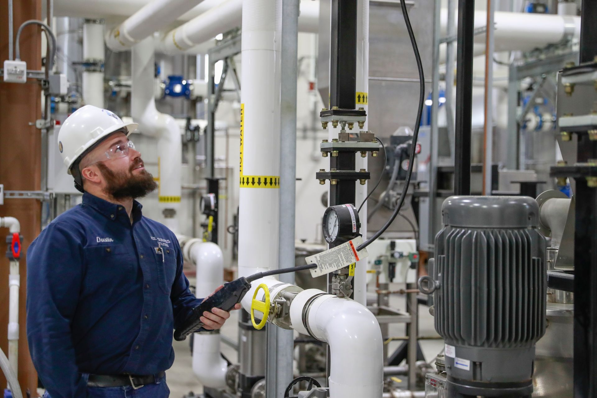 A man in a hard hat is standing in a factory looking at pipes.