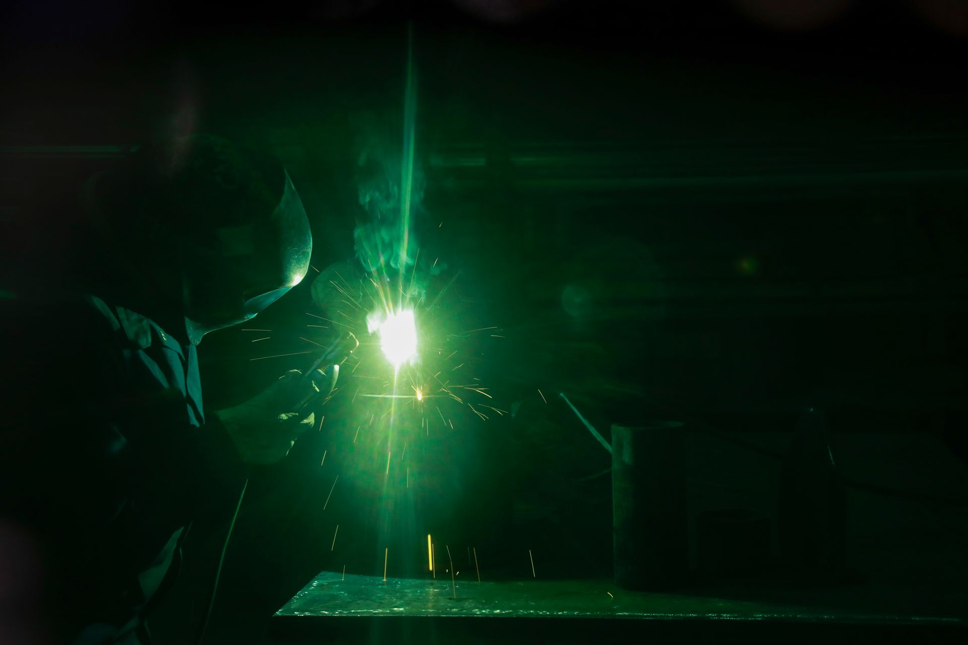 A man is welding a piece of metal in a dark room.