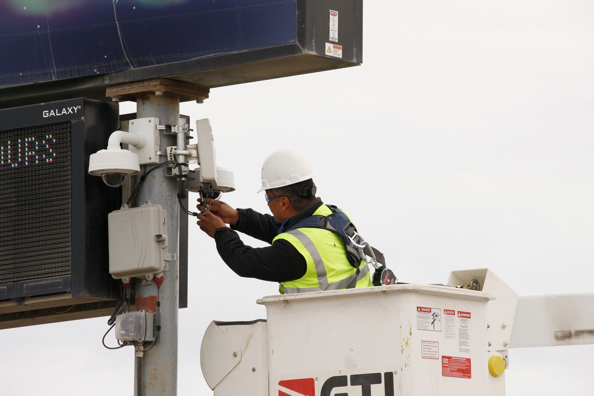 A man in a yellow vest is working on a billboard.