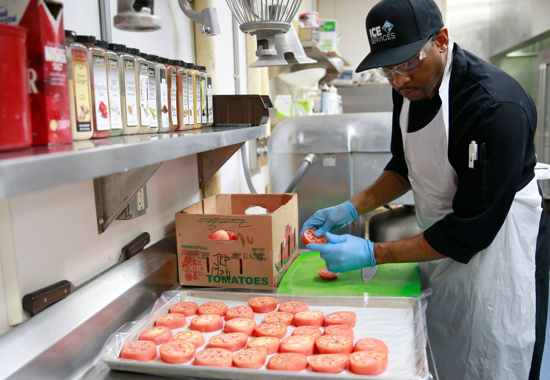 A man is cutting tomatoes in a kitchen with a box of tomatoes in the background